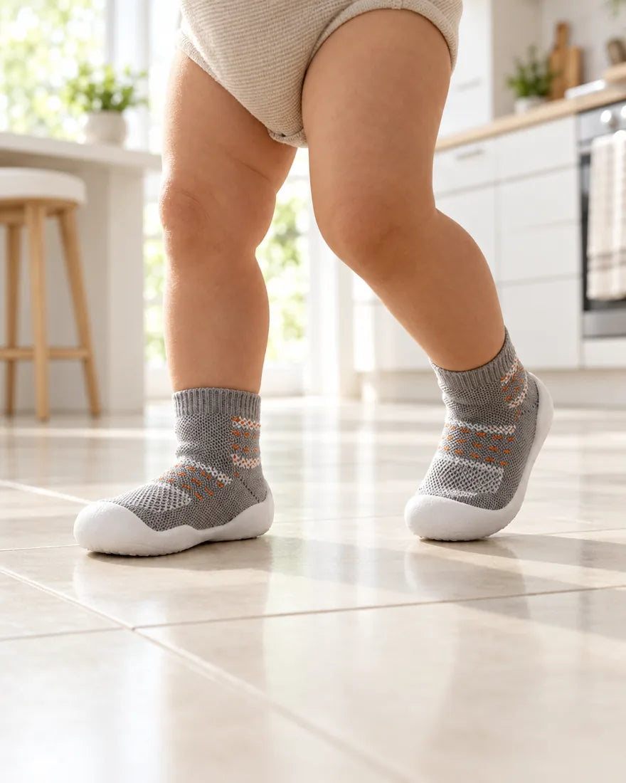 Toddler walking across a kitchen tile floor in Pebble sock shoes